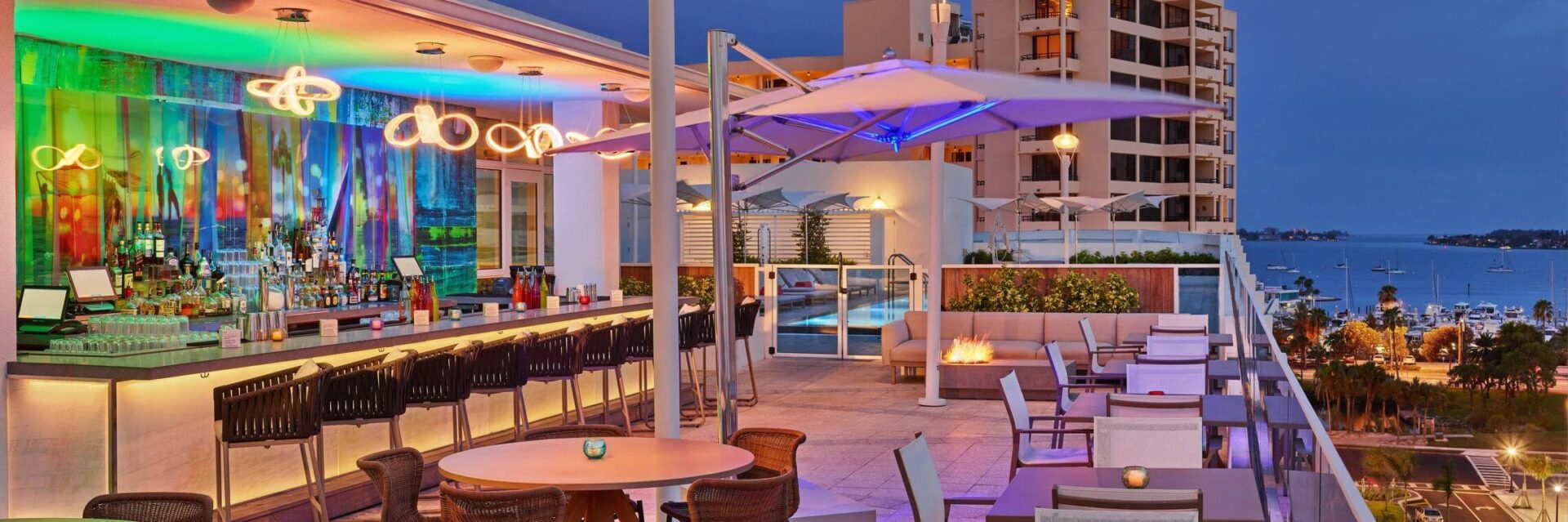 A patio with tables and chairs, pool area and bar.